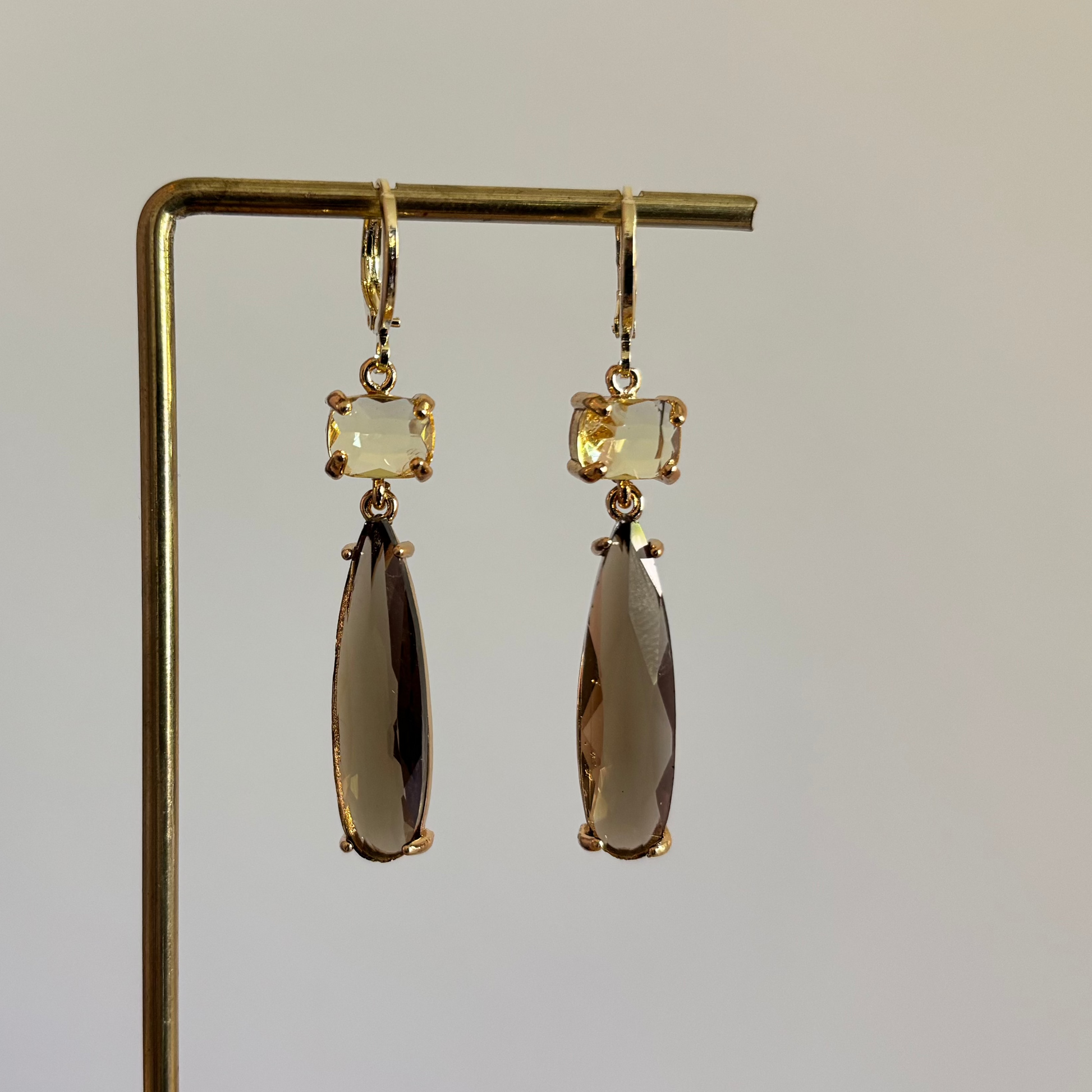 Goudkleurige oorbellen Maya met een kleine rechthoekige gele steen en een lange taupekleurige druppelvormige hanger van kristal