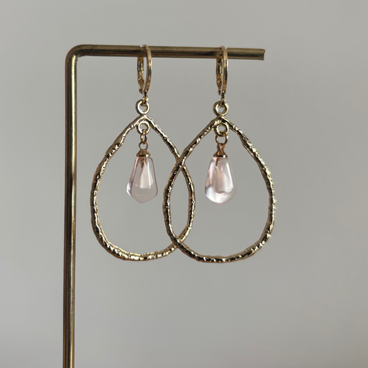 Elegante gouden oorbellen met een 14k verguld ringetje waaraan een open druppelvormige hanger hangt, gecombineerd met een verfijnde acryl druppelbedel voor een zachte glans.