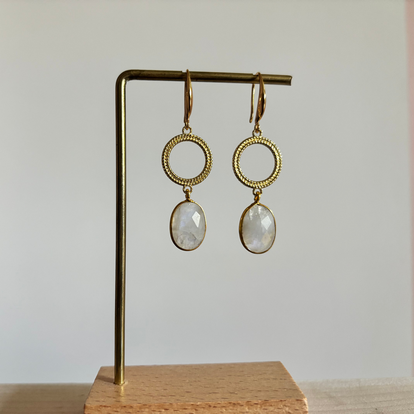Symmetrische goudkleurige oorbellen Mir Maansteen aan een rekje, voorzien van een ronde open ring met textuur en een hangende, ovaal facetgeslepen witte maansteen.