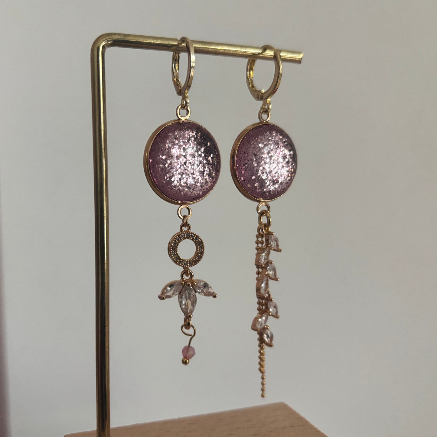 Asymmetrische 14k vergulde oorbellen 'Nina' met glinsterende roze ronde stenen en hangers van heldere kristallen op een gouden standaard.