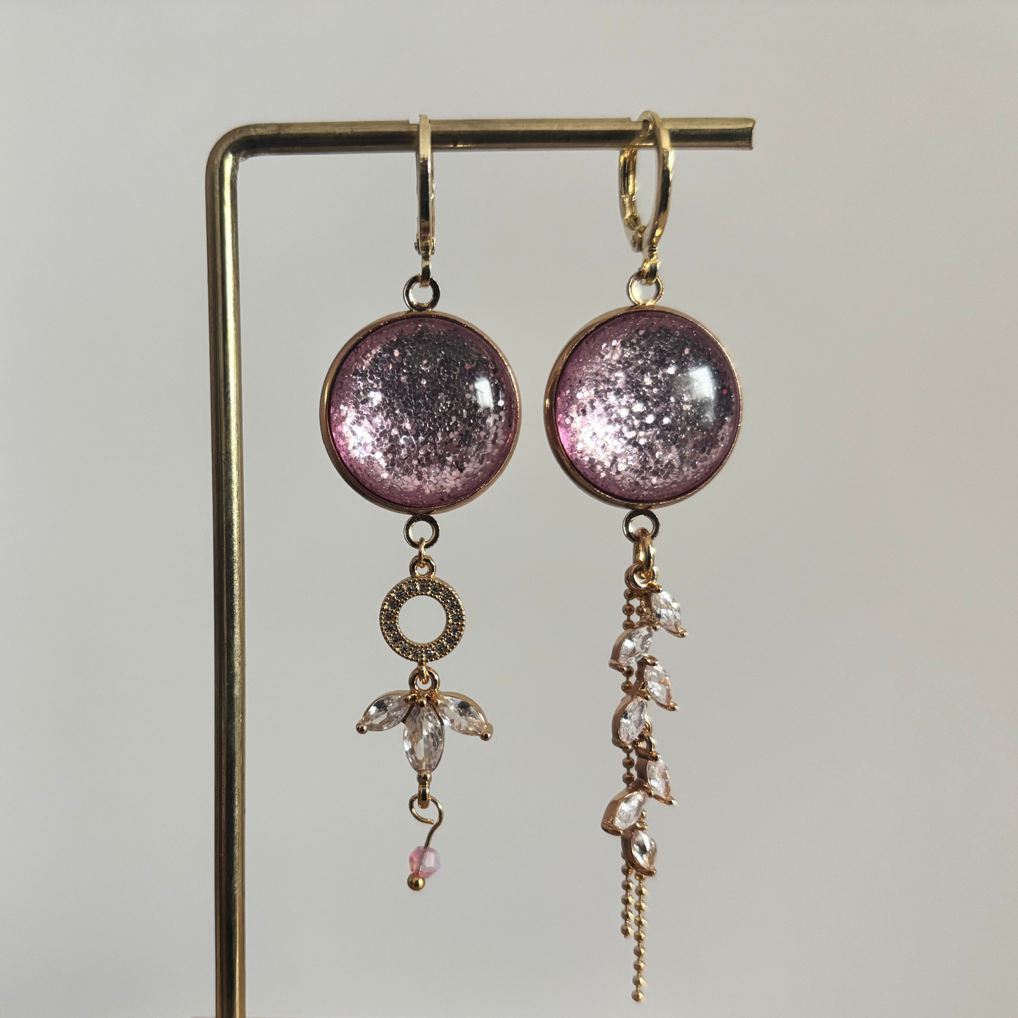 Asymmetrische 14k vergulde oorbellen 'Nina' met glinsterende roze ronde stenen en hangers van heldere kristallen op een gouden standaard.