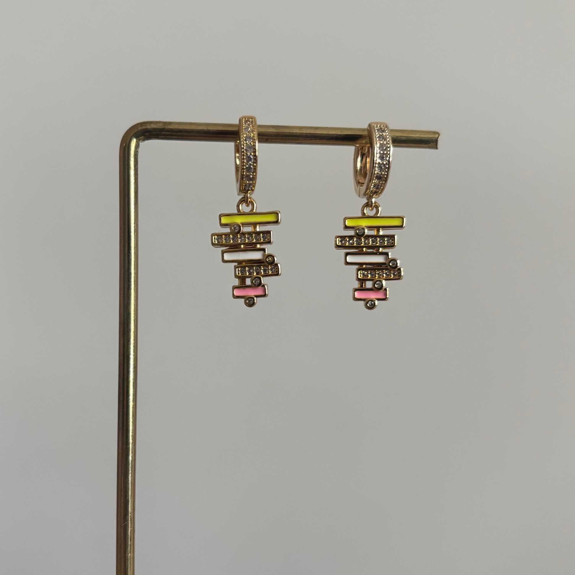 zirkonia oorringen met een hangende bedel van gestapelde geometrische balkjes in geel, wit en roze emaille, bezet met kleine glimmende steentjes.