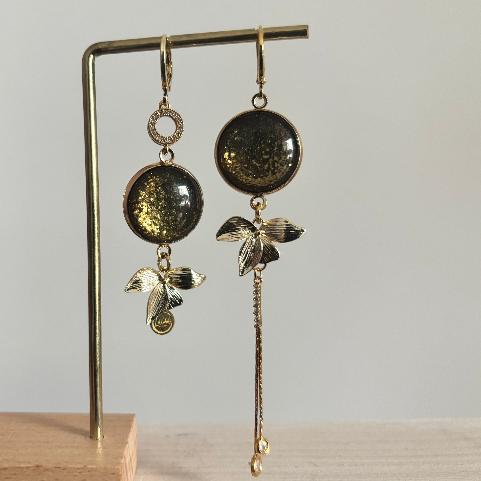 Vergulde asymmetrische oorbellen Olivia met donkergroene stenen en hangers in de vorm van blaadjes.