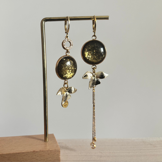 Vergulde asymmetrische oorbellen Olivia met donkergroene stenen en hangers in de vorm van blaadjes.