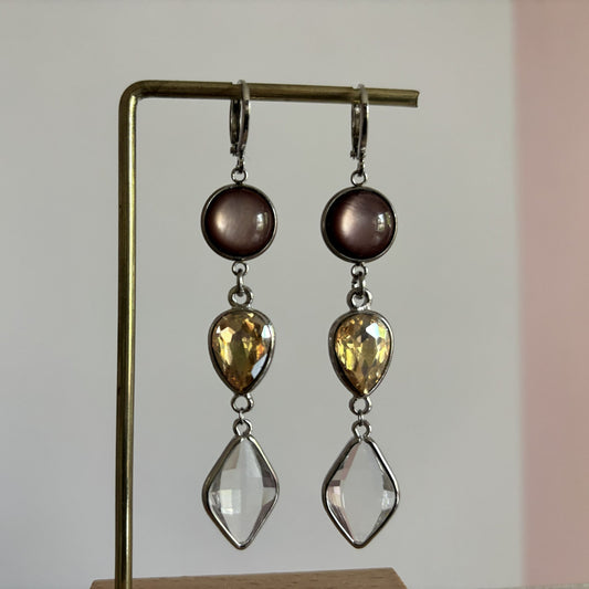 Zilverkleurige oorhangers 'Oukje Bruin' in zilver met een ronde bruine cabochon, een traanvormige amberkleurige glassteen en een heldere ruitvormige hangende steen. 