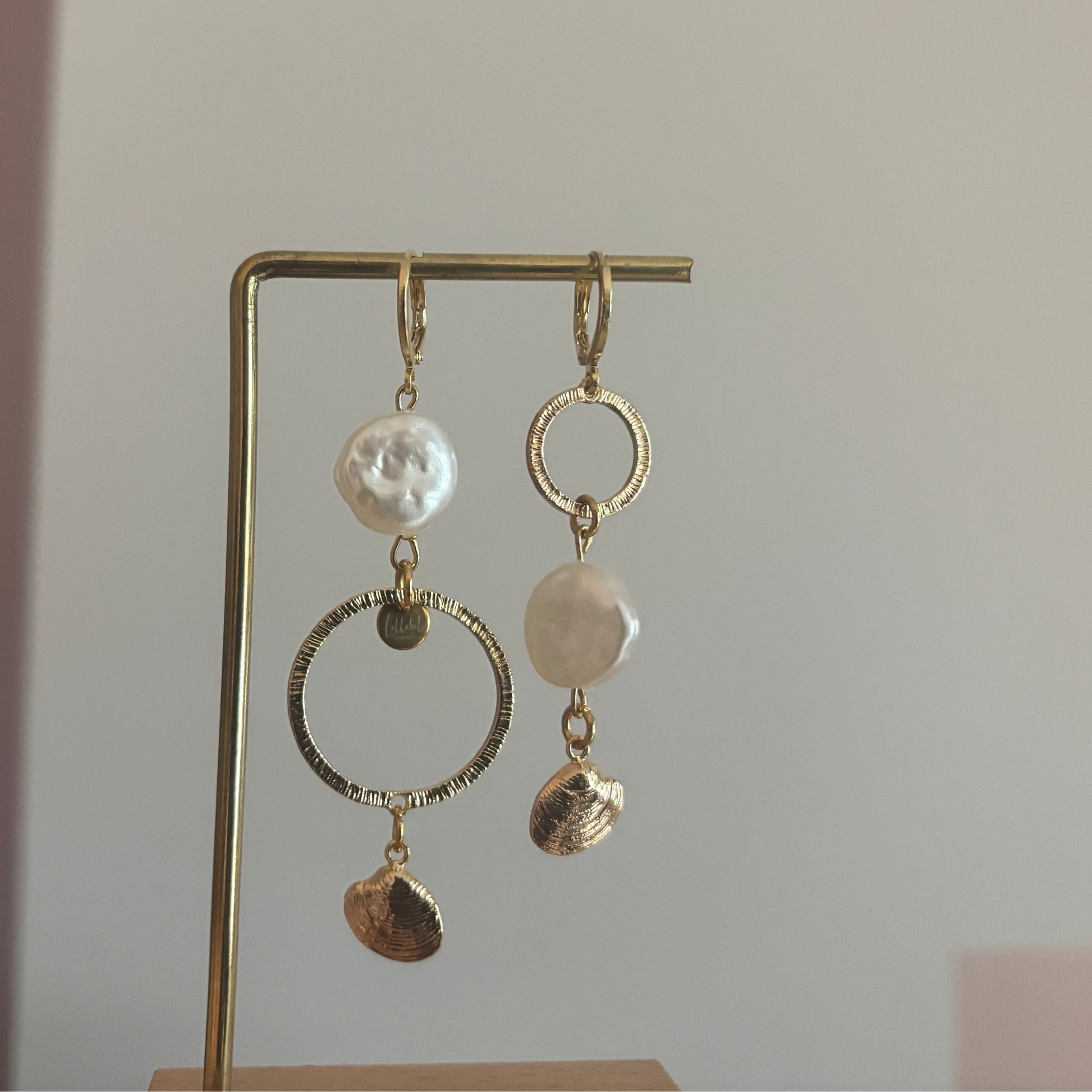 Asymmetrische oorbellen met gehamerde ringen, parel en schelp, circa 6 cm lang.