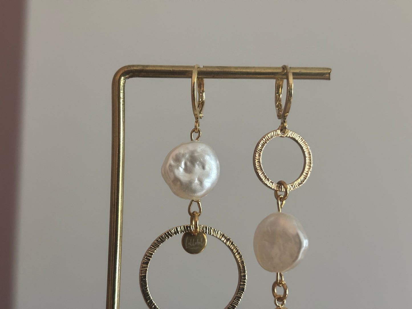 Asymmetrische oorbellen met gehamerde ringen, parel en schelp, circa 6 cm lang.