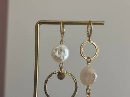 Asymmetrische oorbellen met gehamerde ringen, parel en schelp, circa 6 cm lang.