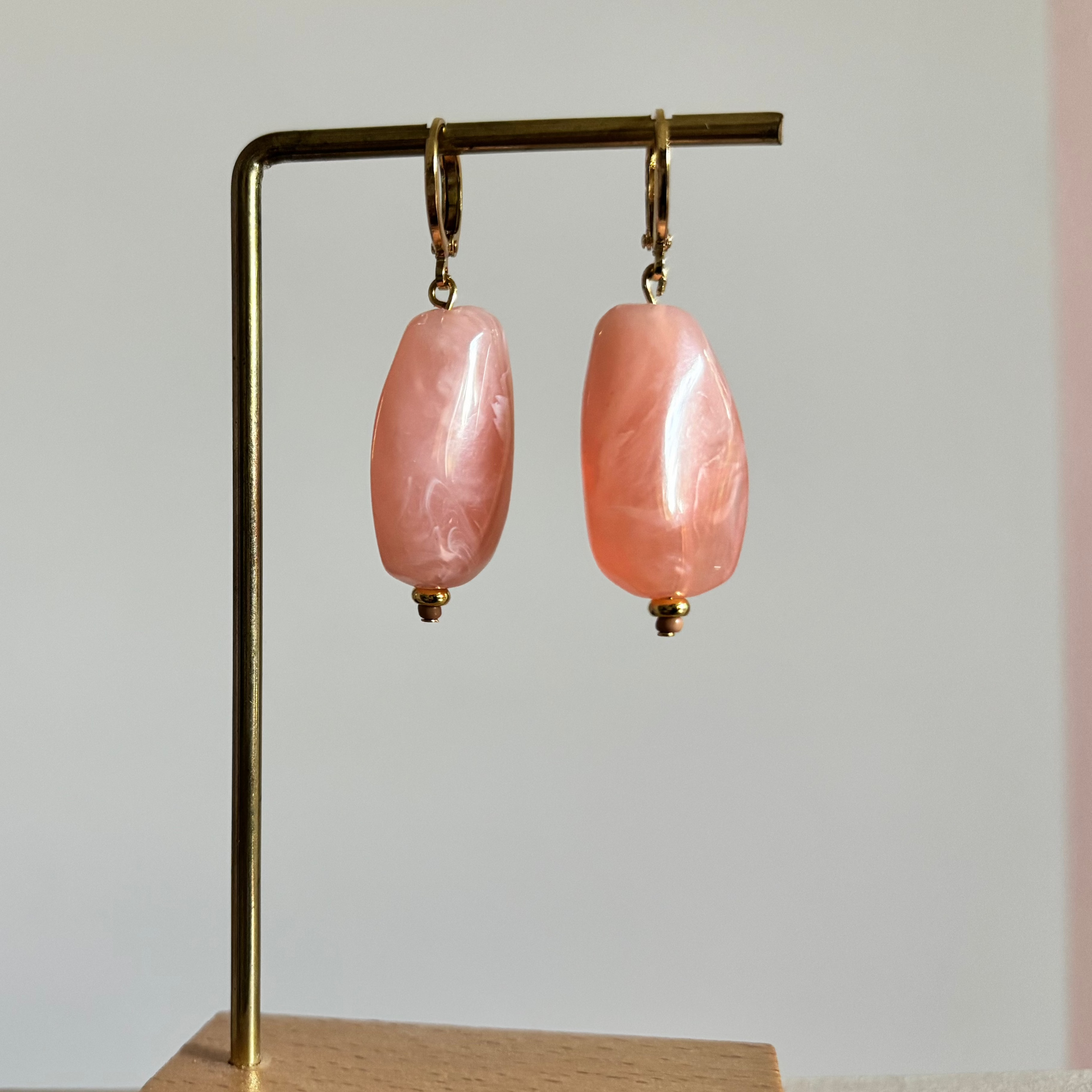 Symmetrische goudkleurige oorbellen Peachy aan een rekje, voorzien van een grote, gladde barokgevormde kraal in een perzikroze tint met parelmoer-effect.
