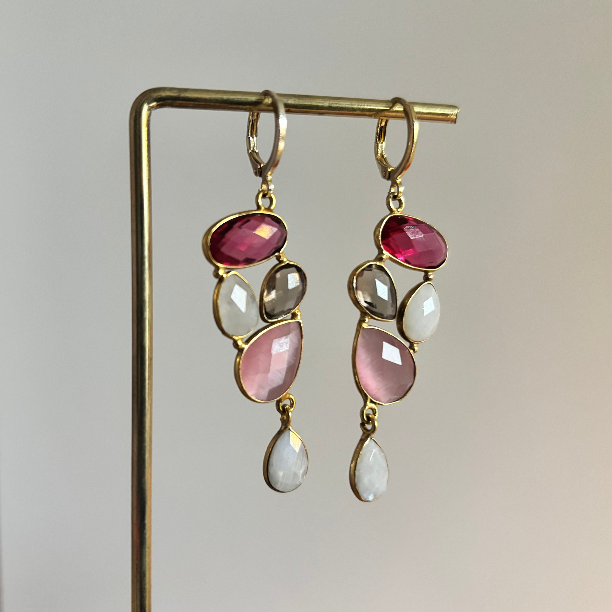 Speelse 14k vergulde oorbellen met een trosje edelstenen in framboosrood, zachtroze, rookkwarts en witte maansteen, licht van gewicht en ca. 5 cm middel­lange lengte.