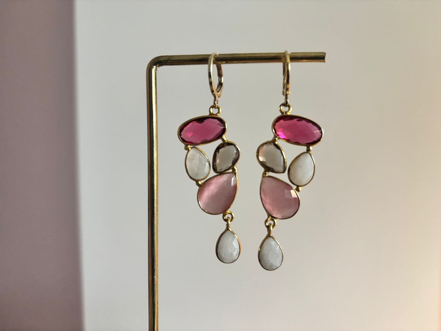 Speelse 14k vergulde oorbellen met een trosje edelstenen in framboosrood, zachtroze, rookkwarts en witte maansteen, licht van gewicht en ca. 5 cm middel­lange lengte.