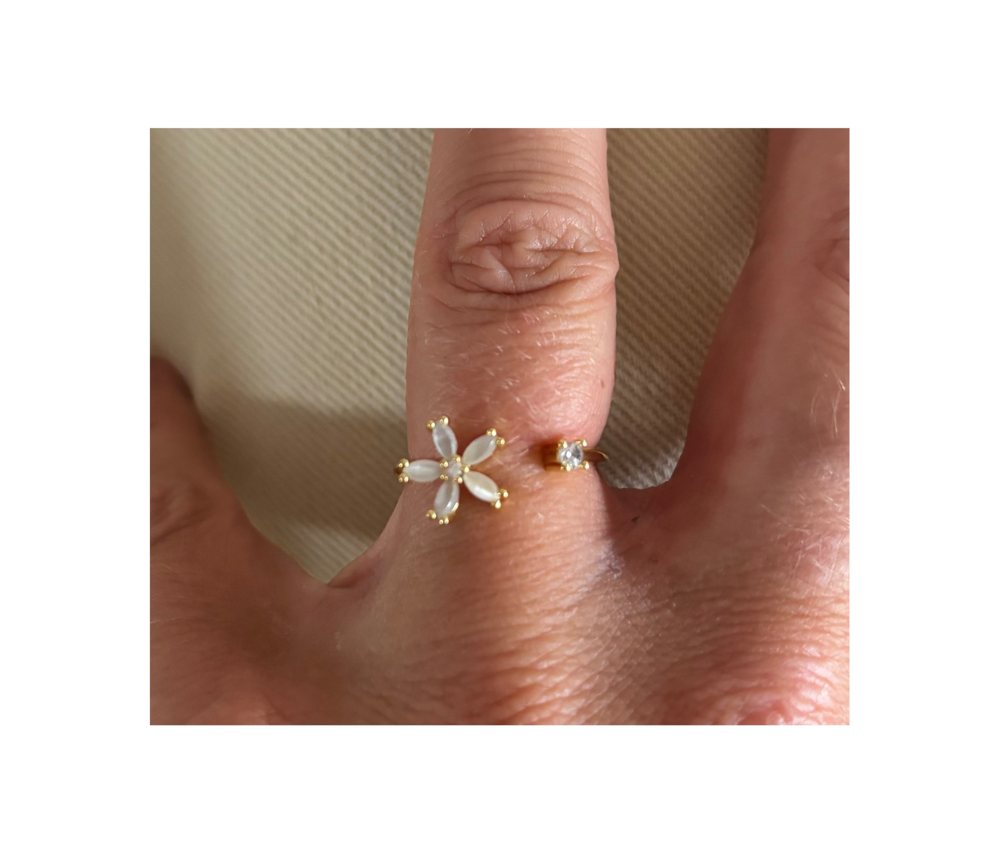 Goudkleurige open ring Bloem gedragen aan een hand, voorzien van een klein wit bloemetje met vijf blaadjes en een tegenoverliggend rond, helder kristalletje.