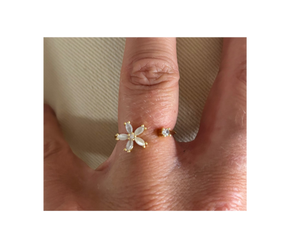 Goudkleurige open ring Bloem gedragen aan een hand, voorzien van een klein wit bloemetje met vijf blaadjes en een tegenoverliggend rond, helder kristalletje.