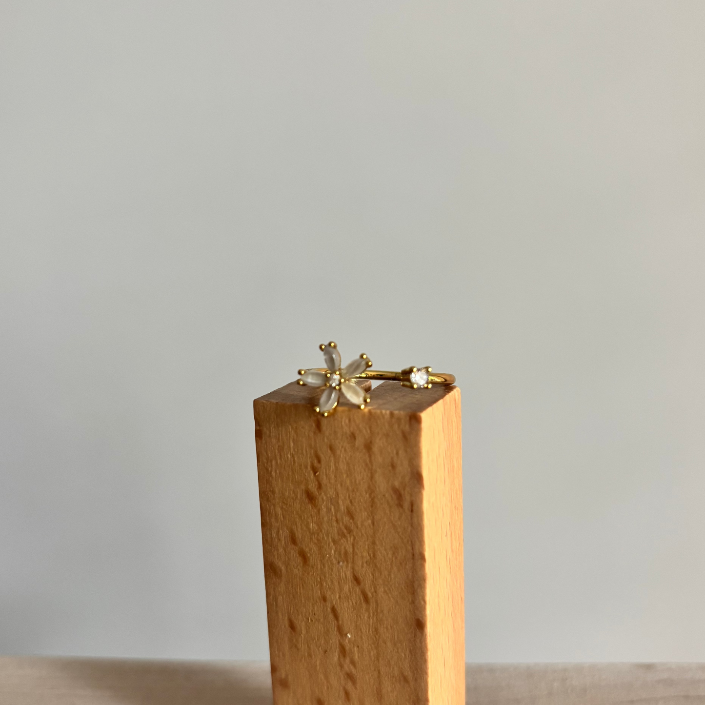 Goudkleurige open ring Bloem gedragen aan een hand, voorzien van een klein wit bloemetje met vijf blaadjes en een tegenoverliggend rond, helder kristalletje.