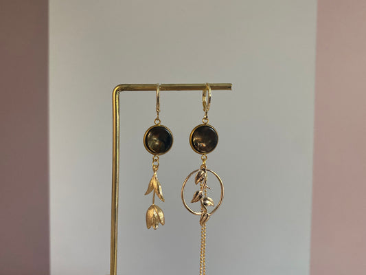 Asymmetrische 14k vergulde oorbellen met donkerbruine cabochons, tulp aan de ene kant en plantenhanger met kwastje aan de andere kant.