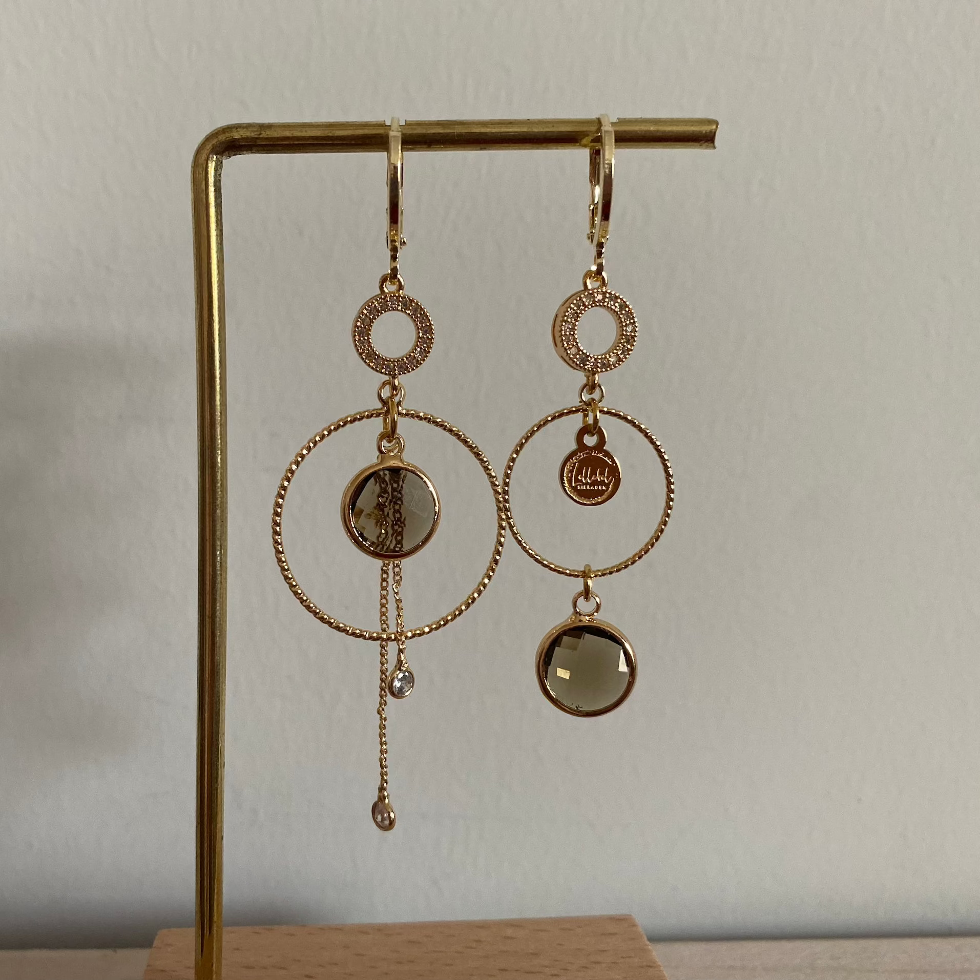 Een productfoto van het ongelijke paar Lellebel Oorbellen "Sandra", met zirkonia hangers en taupe kleurige glasbedels.