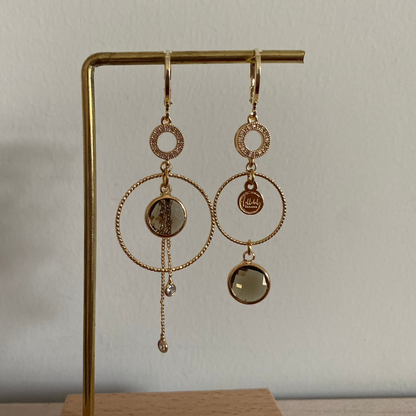 Een productfoto van het ongelijke paar Lellebel Oorbellen "Sandra", met zirkonia hangers en taupe kleurige glasbedels.