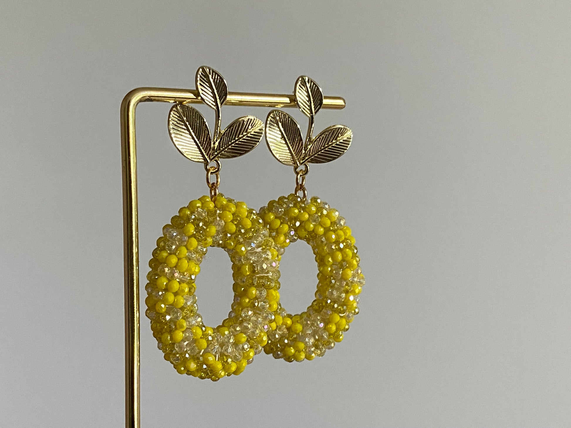 Handgemaakte bold statement oorbel met gele kralenhanger en een 14K vergulde gouden bladsteker.
