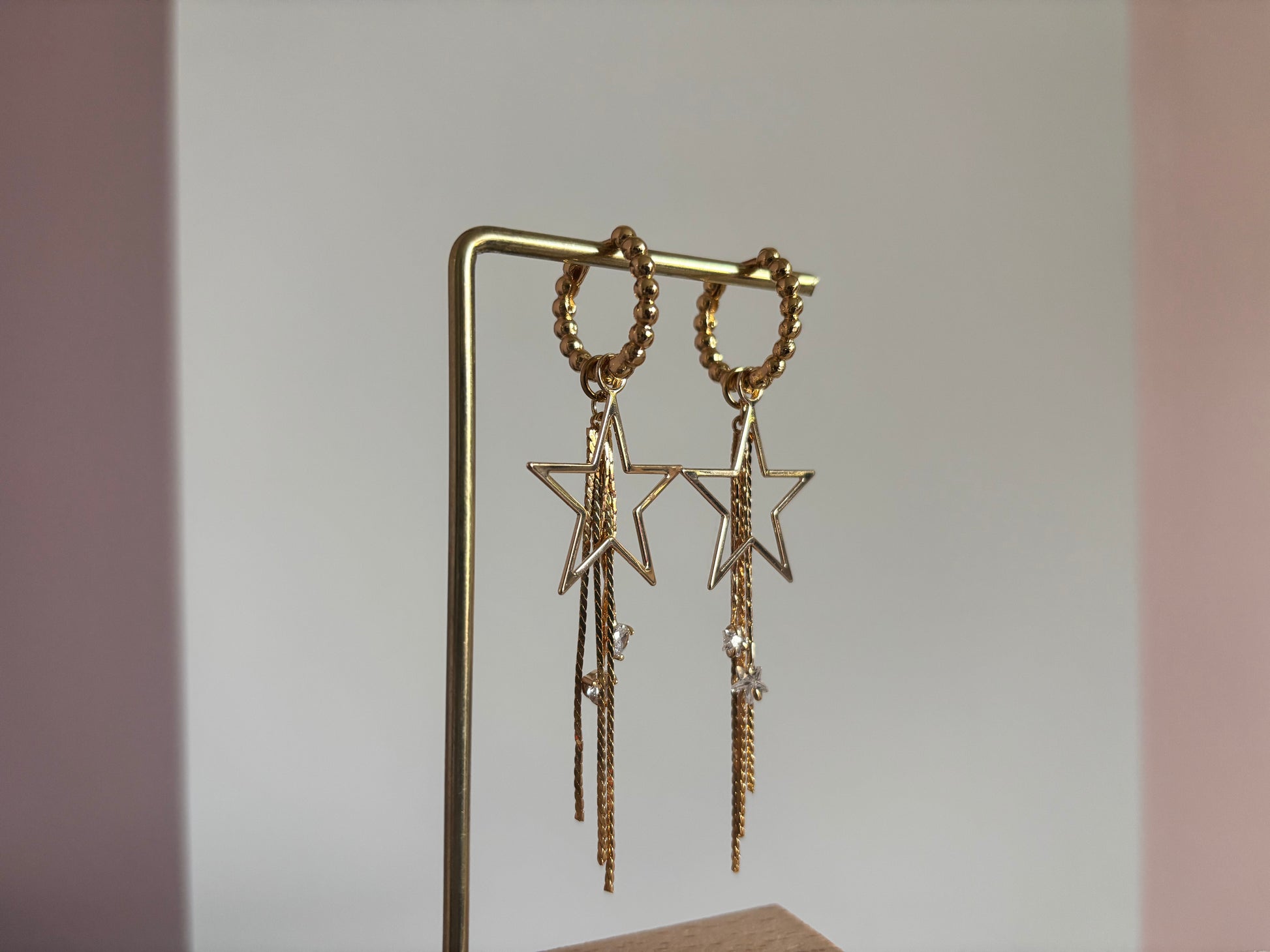 14k vergulde oorbellen 'Sterre' van Lellebel op een standaard. De oorbellen hebben een goudkleurige ster met daaraan hangende fijne kettinkjes en kleine glanzende zirkonia steentjes.
