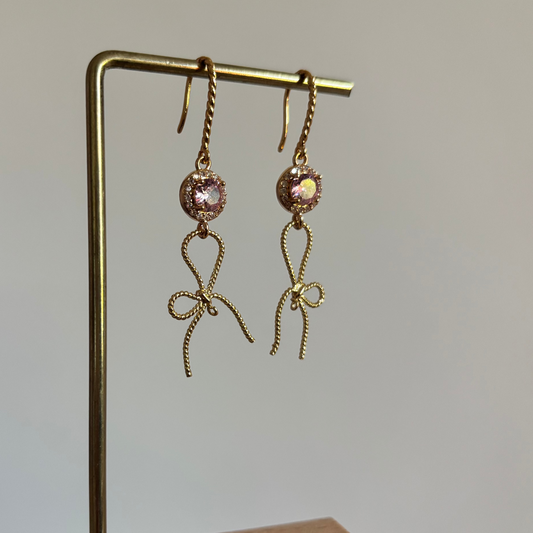 "Gouden oorhangers Strikkie Roze met gedraaide haakjes, een ronde lichtroze zirkonia met strass-rand en een gedraaid gouden strikje