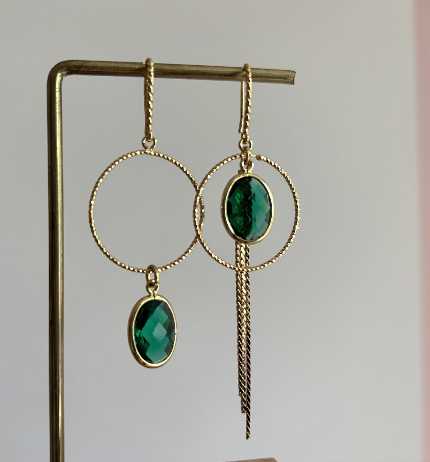 Goudkleurige asymmetrische oorbellen Toos met bewerkte ronde ringen, ovale gefacetteerde groene kristallen en een lang neerhangend kettinkje.