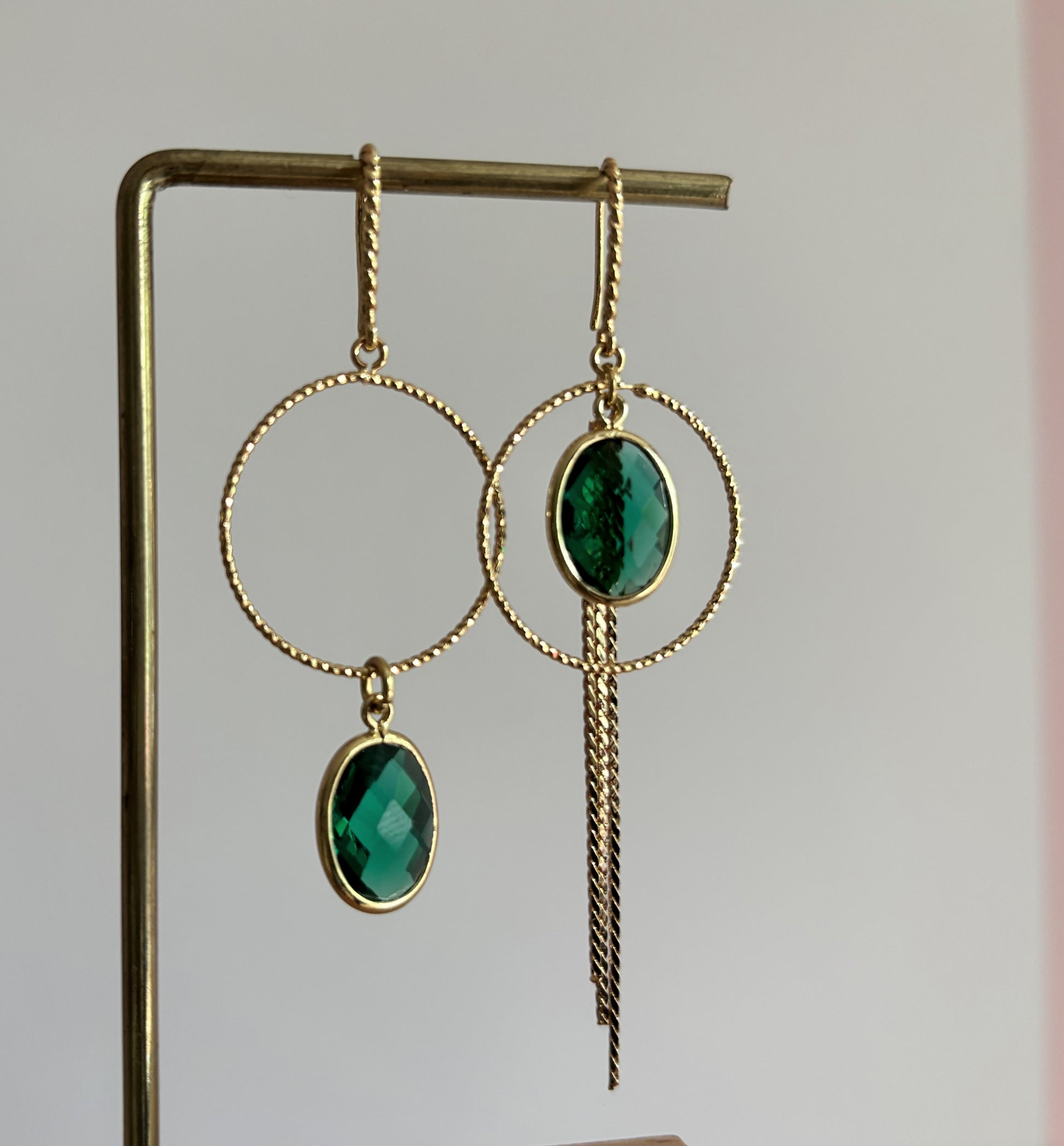 Goudkleurige asymmetrische oorbellen Toos met bewerkte ronde ringen, ovale gefacetteerde groene kristallen en een lang neerhangend kettinkje.