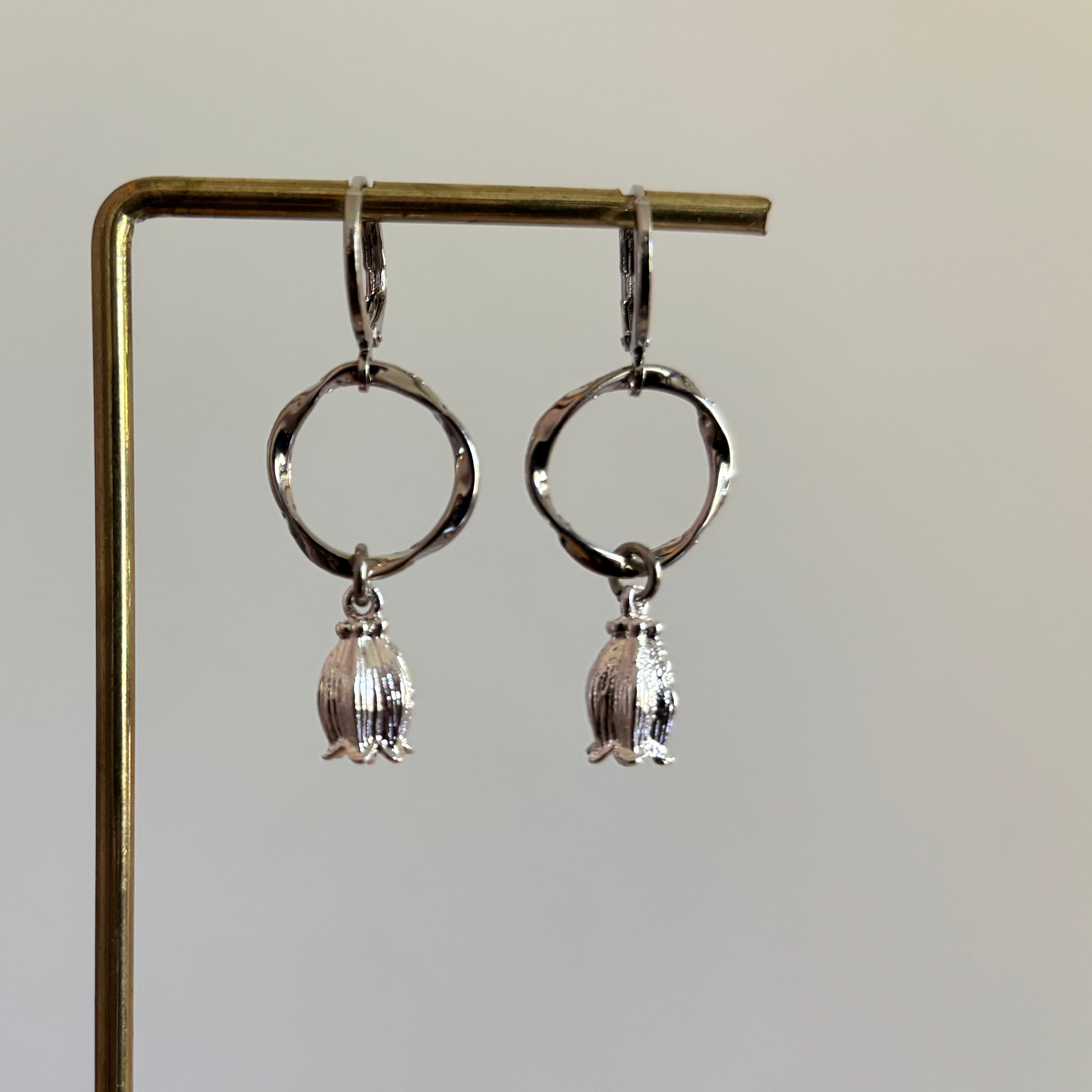 "Zilverkleurige oorbellen met een gedraaide ronde hanger en een kleine, gedetailleerde tulpbedel aan de onderzijde."