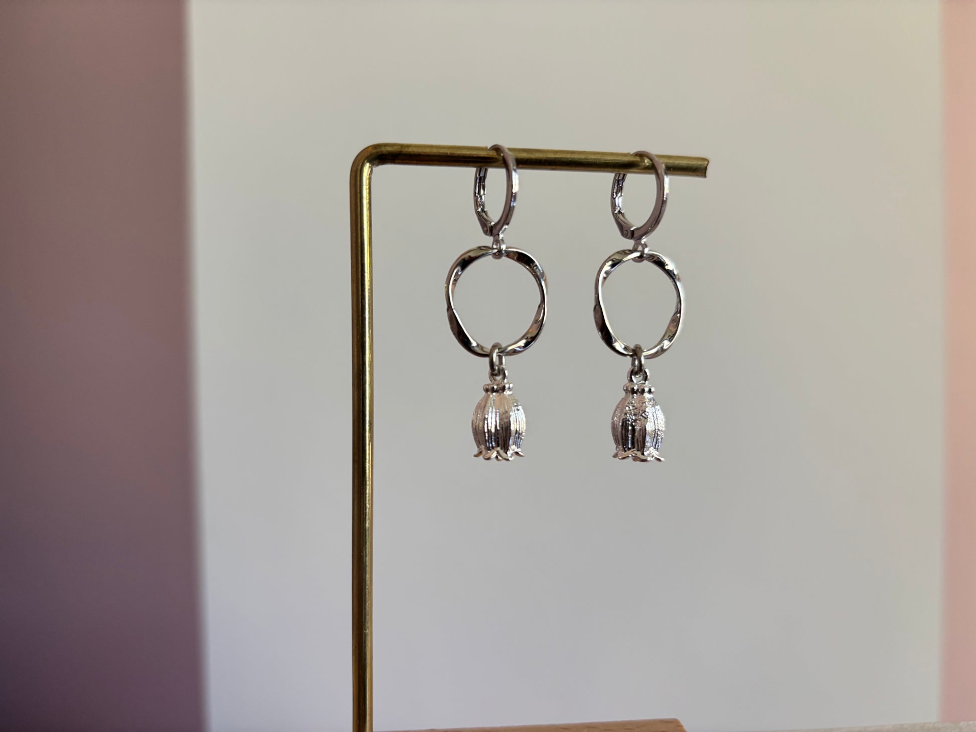 "Zilverkleurige oorbellen met een gedraaide ronde hanger en een kleine, gedetailleerde tulpbedel aan de onderzijde."