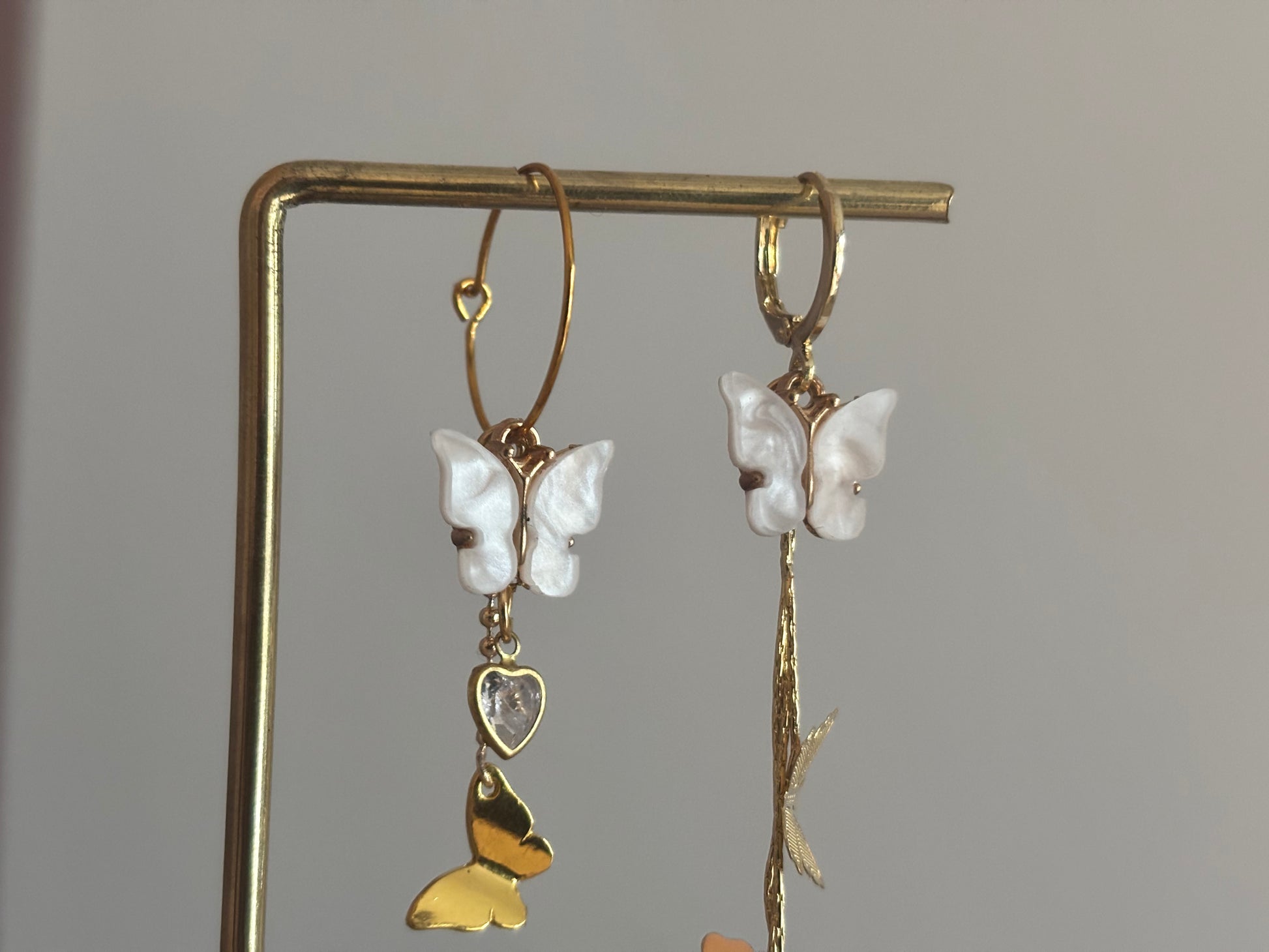 Asymmetrisch paar met 14K vergulde vlinderstreng, Shell vlinders en een mini glazen hartjesbedel, aan een 14K gouden oorringetje