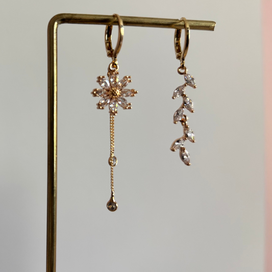 Asymmetrische 14k vergulde oorbellen Wies. Links een zirkonia bloem met twee fijne kettinkjes, rechts een takje van zirkonia blaadjes, hangend aan een rekje.