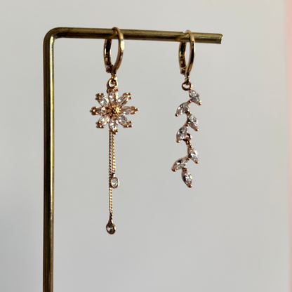 Asymmetrische 14k vergulde oorbellen Wies. Links een zirkonia bloem met twee fijne kettinkjes, rechts een takje van zirkonia blaadjes, hangend aan een rekje.