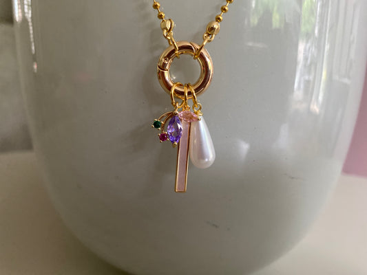 Close-up van RVS bolletjes ketting met daaraan een connector met  3 bedels: een Maple blad, een staafjesbedel van shell en een parel.