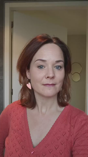 Filmpje van model met Asymmetrisch paar met links een emaille hart en rechts 14K vergulde bedels en zirkonia afgewisseld met een emaille bedel in koraal
