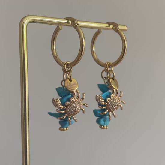 Filmpje van 18K vergulde krab ingelegd met zirkonia hangend aan een oorbel met rvs hoops en turquoise natuurstenen