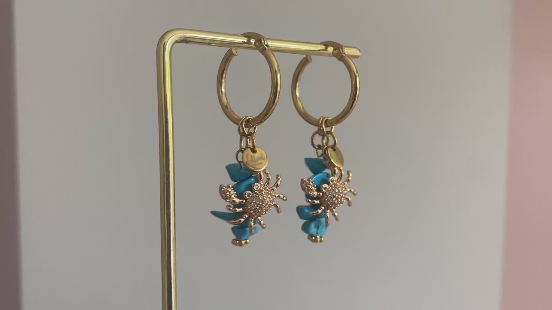 Filmpje van 18K vergulde krab ingelegd met zirkonia hangend aan een oorbel met rvs hoops en turquoise natuurstenen