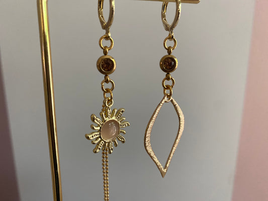 detailfoto van Asymmetrische oorbellen van 14K verguld goud met een zon van een cateye steen en een gehamerde 14K vergulde druppelvormige hanger en dieporanje zirkonia bedeltjes.